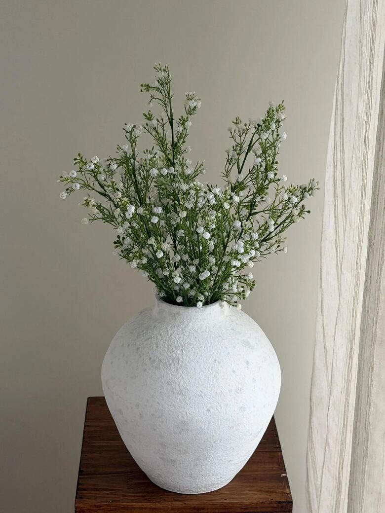 Artificial white gypsophila stems arranged in a textured white ceramic vase