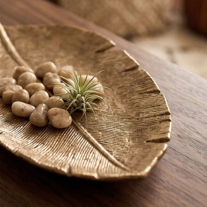 Close-up of a gold leaf-shaped tray holding small pebbles and a miniature air plant