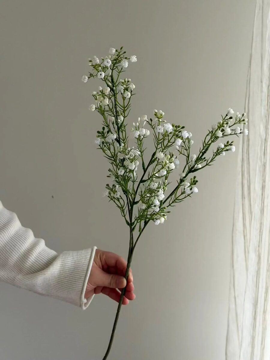 Hand holding a single artificial white gypsophila baby's breath stem