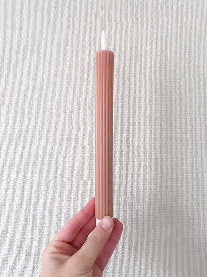 Hand holding a blush pink ribbed flameless LED taper candle against a textured wall