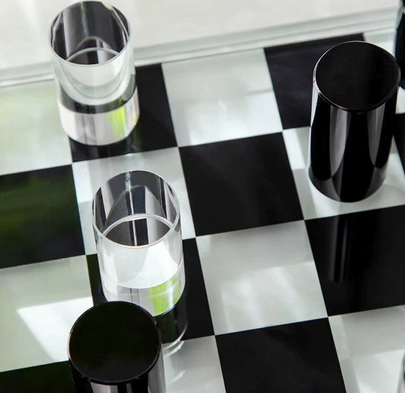 Four drinking glasses arranged on a glossy black-and-white checkered surface. Three glasses are clear and one is opaque black.