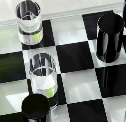 Four drinking glasses arranged on a glossy black-and-white checkered surface. Three glasses are clear and one is opaque black.