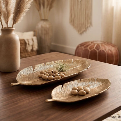 Two gold leaf-shaped trays with almonds and an air plant on a wood table, styled with dried pampas grass and a leather pouf