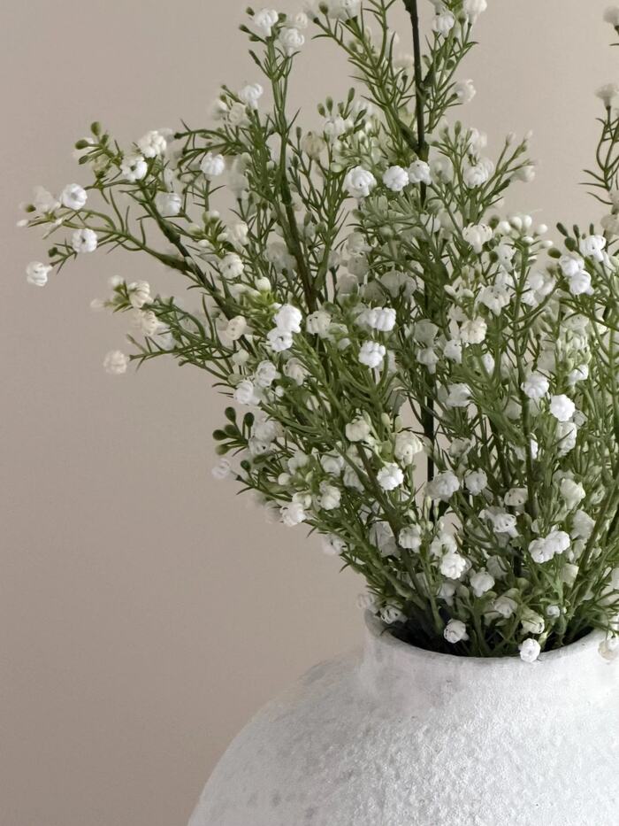 Close-up of artificial white gypsophila blooms and foliage in a textured vase