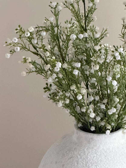 Close-up of artificial white gypsophila blooms and foliage in a textured vase
