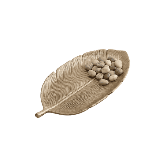 Gold leaf-shaped decorative tray holding small white and grey pebbles, on a light stone windowsill